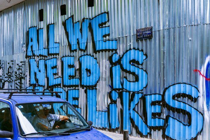 Car beside a wall of graffiti that reads "All We Need Is More Likes"