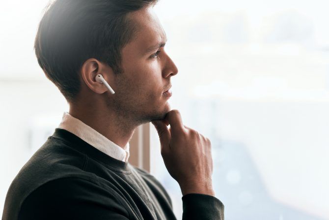 Man thinking while he looks out of window wearing wireless in ear headphones