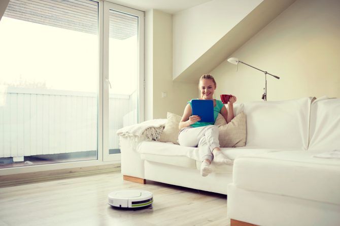 Woman relaxing on sofa drinking tea while robot vacuum cleans